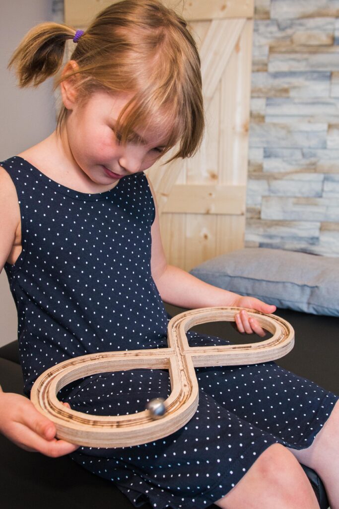 Kind hält hölzerne Acht-Bahn (∞) mit Kugel – spielerische TFH-Übung zur Koordination und Konzentration.