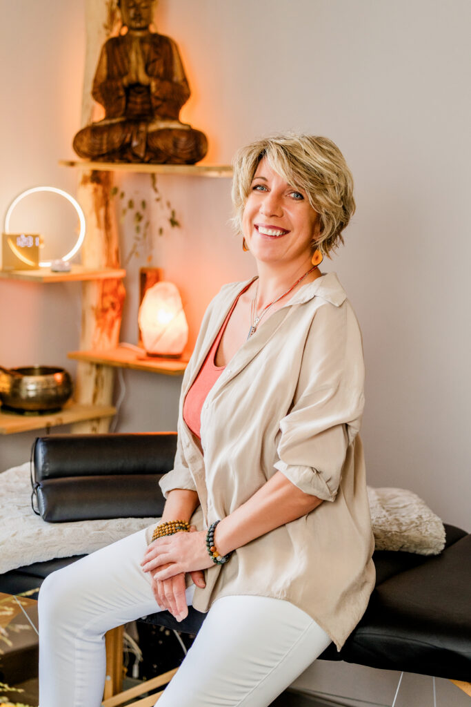 Lächelnde Therapeutin auf Behandlungsliege in warm beleuchteter Kinesiologie-Praxis in Ebersbach – Über-mich.